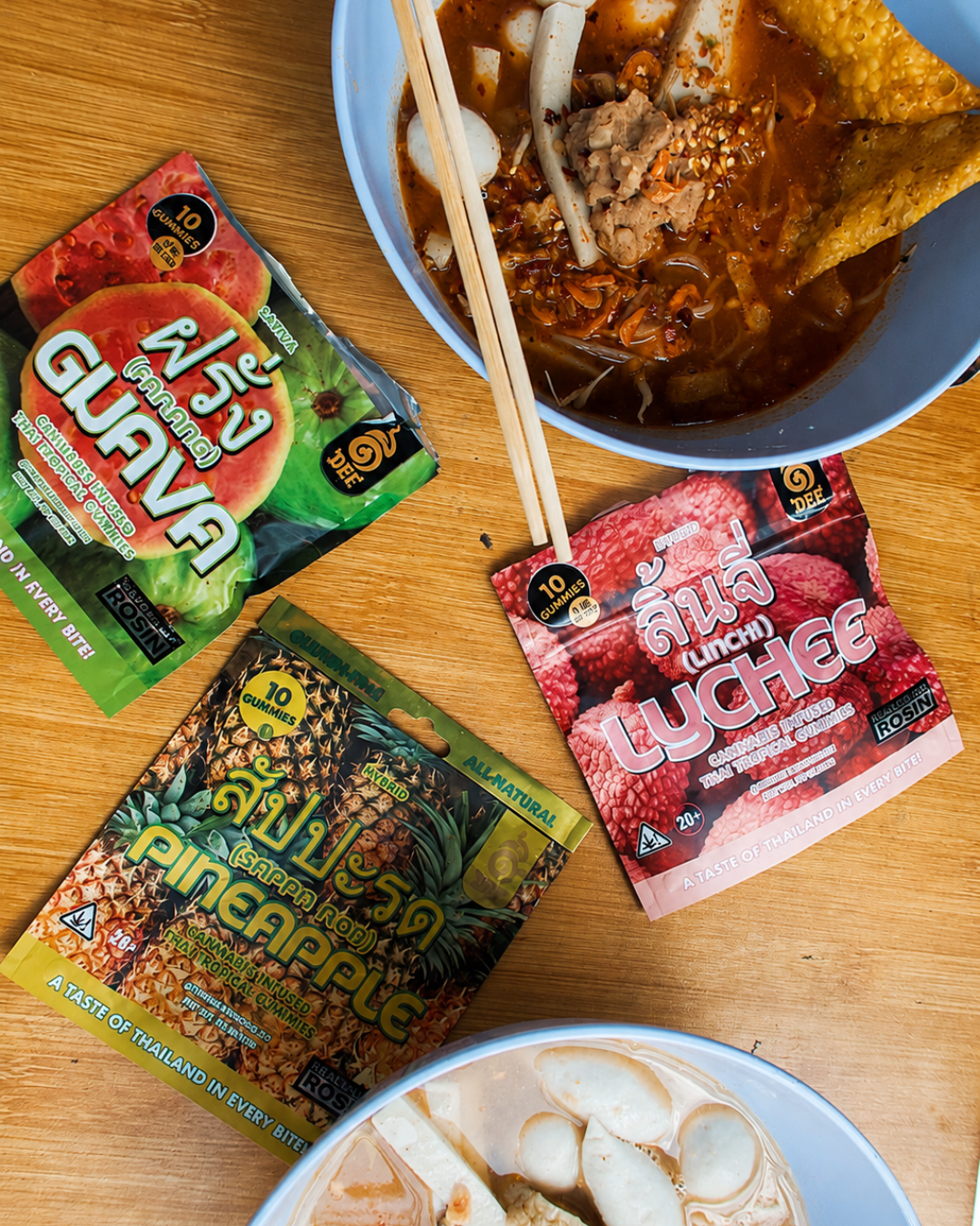 Dee Thai gummy packs arranged around Thai noodle bowls